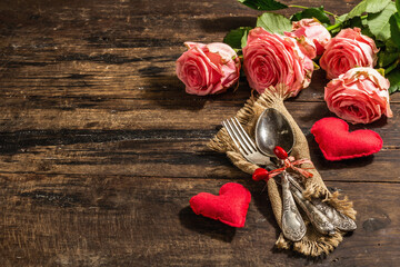 Rustic table setting for romantic dinner. Bouquet of fresh roses, cutlery and heart