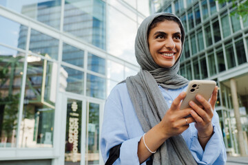 Fototapeta premium Young muslim businesswoman using cellphone while walking outdoors