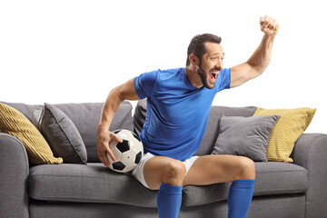 Obraz premium Football player sitting on a sofa holding a ball and watching a match