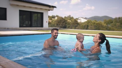 Family playing with baby child in outdoor swimming pool.