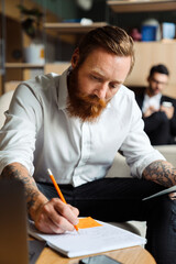 Businessman sitting in office with his colleague on a background writing down notes