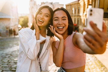 Two young beautiful smiling happy asian girls taking selfie - obrazy, fototapety, plakaty