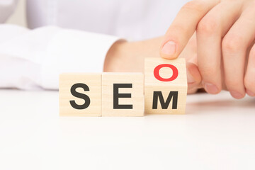Hand flip SEO to SEM text wooden cube blocks on table background. search engine optimization, advertising, idea, strategy, marketing concept