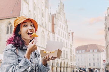 Cheerful happy girl snacking on fast food with shrimp in batter on the street of the city of Munster in Germany in a takeaway paper box - obrazy, fototapety, plakaty