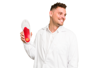 Young caucasian chiropodist man isolated looks aside smiling, cheerful and pleasant.