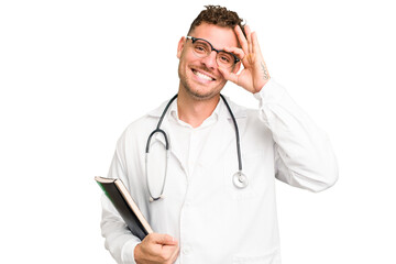 Young doctor caucasian man holding a book isolated excited keeping ok gesture on eye.
