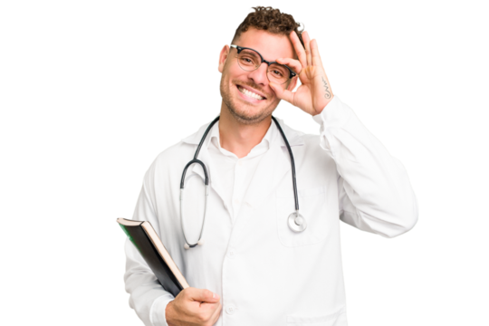 Young doctor caucasian man holding a book isolated excited keeping ok gesture on eye.