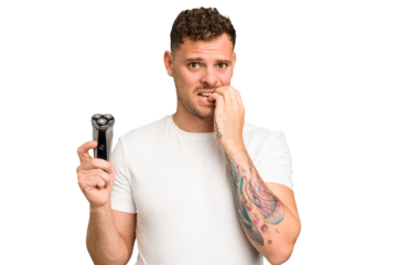 Young caucasian man holding a razor isolated biting fingernails, nervous and very anxious.