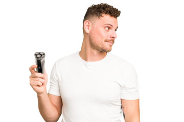 Young caucasian man holding a razor isolated looks aside smiling, cheerful and pleasant.