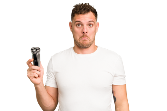 Young caucasian man holding a razor isolated shrugs shoulders and open eyes confused.
