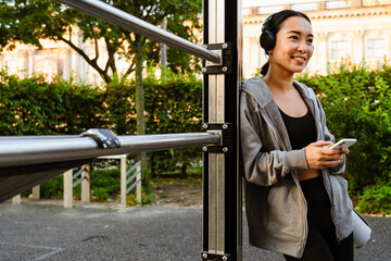 Young asian woman in headphones using cellphone on playground