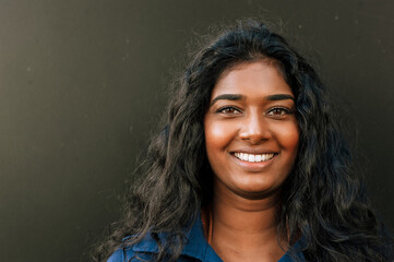 Young indian woman smiling at camera while standing over dark background