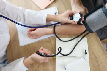 Female doctor using sphygmomanometer checks patient's blood pressure in medical clinic.