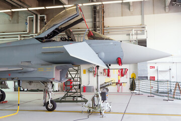 European modern military air force fighter jet in a hangar on an air base. - obrazy, fototapety, plakaty