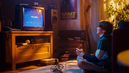 Young Boy Playing 80s Eight Bit Arcade Space Shooter Video Game on a Console at Home in His Vintage...