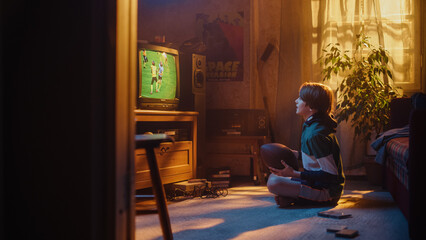 Young Sports Fan Watches American Football Match on Retro TV in His Room with Dated Interior. Boy...