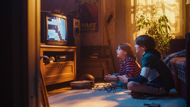 Nostalgic and Happy Childhood Concept: Young Brother and Sister Playing 8 Bit 2D Arcade Video Game on a Retro TV Set at Home in a Room with Period-Correct Interior. Friends Completing the Level.