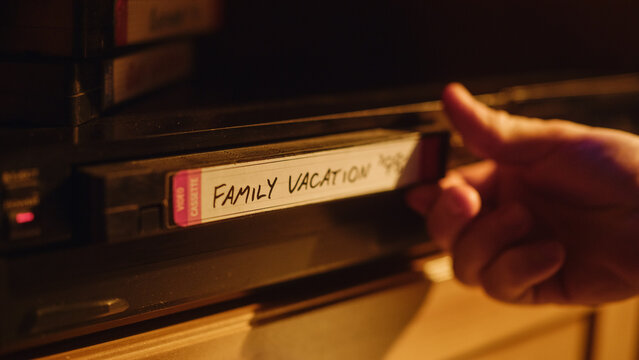 Close Up of a Person Inserting a VHS Cassette in a Player with Happy and Nostalgic Vacation Footage from Home Video Camera. Retro Nineties Technology. Old VCR with Shallow Depth of Field and Bokeh.
