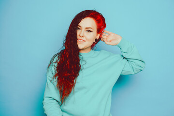 Woman in a blue sweater on a blue background posing. A beautiful brunette with long hair and and tunnels in her ears. Eyeliner and trendy makeup.