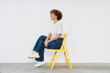 Middle-aged woman sitting on yellow chair and looking away isolated