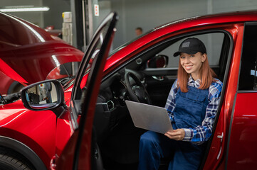 Naklejka premium Woman auto mechanic doing diagnostics in car using laptop. 