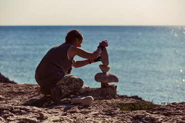 Woman balancing stones on the ocean sea coast.