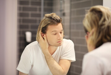 young man looking in the mirror,combing his hair,looking at problems on face.