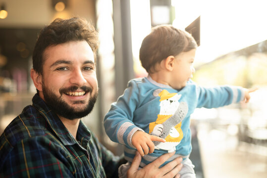 Bearded man with baby son in bar near to window looking at camera