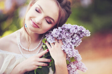 Beautiful fair-haired girl in a vintage look, in a spring park near a lush purple lilac bush, with a bouquet in her hands, close-up portrait