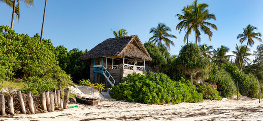 Am Strand der Matemwe Beach auf der Insel Sansibar. Ein traditionelles Holzhaus, ein Fischerboot und Palmen auf der karibischen Insel und ein blauer Himmel, Panorama.