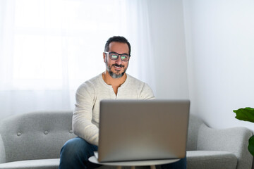 man with black hair using laptop at home sofa