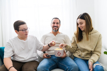 father teen girl and boy watching television while eating pop corn at home
