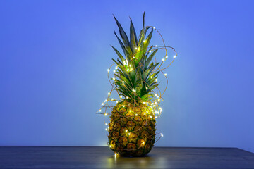 Pineapple with Christmas led-light garland on table, copy space. Zero-waste Christmas decor