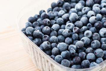 Close up shot of frozen blueberries in transparent plastic tray on white wooden table. Vegetarian, healthy nutrition, food from summer for winter