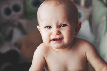 Frowning little kid looking at camera from infant cot at nursery. Displeased wrinkled baby with...