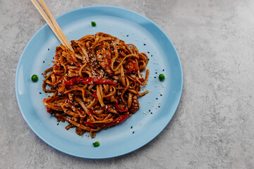 Spicy udon with chicken on a blue plate on a gray concrete background. Top view