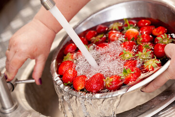 Fresh strawberries being washed in a sink under the tap of the water splashing around with shiny air bubbles and looking very fresh and clean