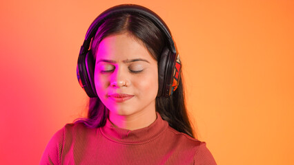 Beautiful young woman listening music with wireless headphones on her head, happy teenage girl enjoying music isolated over colour background