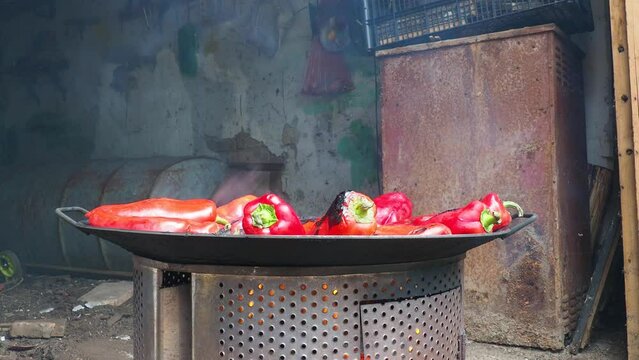 Roasting red peppers for a smoky flavor and quick peeling. Thermal processing of the pepper crop on a metal circle. Brazier container used to burn charcoal fuel for cooking, heating or cultural