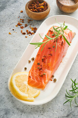 Salmon fish piece. Fresh raw salmon fish piece on marble board stand with herbs and lemon on light grey background. Seafood or menu concept. Top view.
