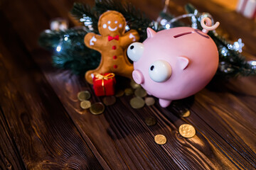 Obraz premium Piggy bank on a twin farm table with scattered coins and garlands with lights. Christmas decor. Spending on New Year's holidays.
