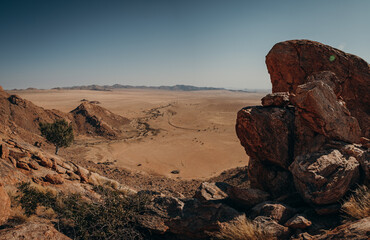 Fototapeta na wymiar Blick von einem Gipfel der Aus-Berge in weite Ebene der Namibia Wüste - eine kleines Farmhaus im Vordergrund (Aus, Namibia)