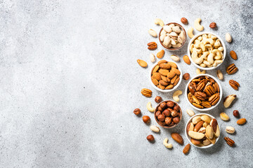 Assortment of nuts in bowls. Cashew, hazelnuts, pecan, almonds, brazilian nuts and pistachios at light table. Top view with copy space.