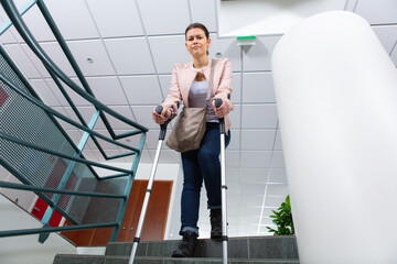 young woman going down the stairs by herself using crutches