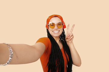 Young woman with box braids is taking a selfie while showing v gesture.