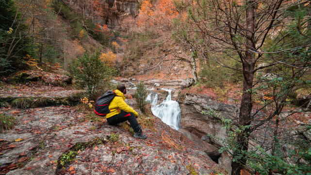 High resolution photograph of a boy admiring the landscape of the Bellos River in the Añisclo Canyon in the Ordesa y Monte Perdido National Park in the Autumn season, with orange beech and pine trees 