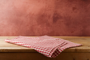 Empty wooden table with red checked tablecloth over rustic wall  background. Kitchen interior mock...