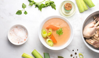 Basic bone and chicken  broth bowl    with parsley, leek, bay leaf and black pepper on a white background. Winter base for hot recipes: soups, risottos, pastas and sauces. Top view