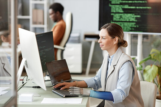 Smiling woman with bionic arm coding on computer when working on big project at research center