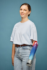 Portrait of smiling young woman in jeans and white t-shirt clenching prosthetic fist